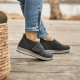 Nainen yllään antrasiitinharmaat New Feet tossut puulattialla, sivukuva keskittyen jalkoihin
